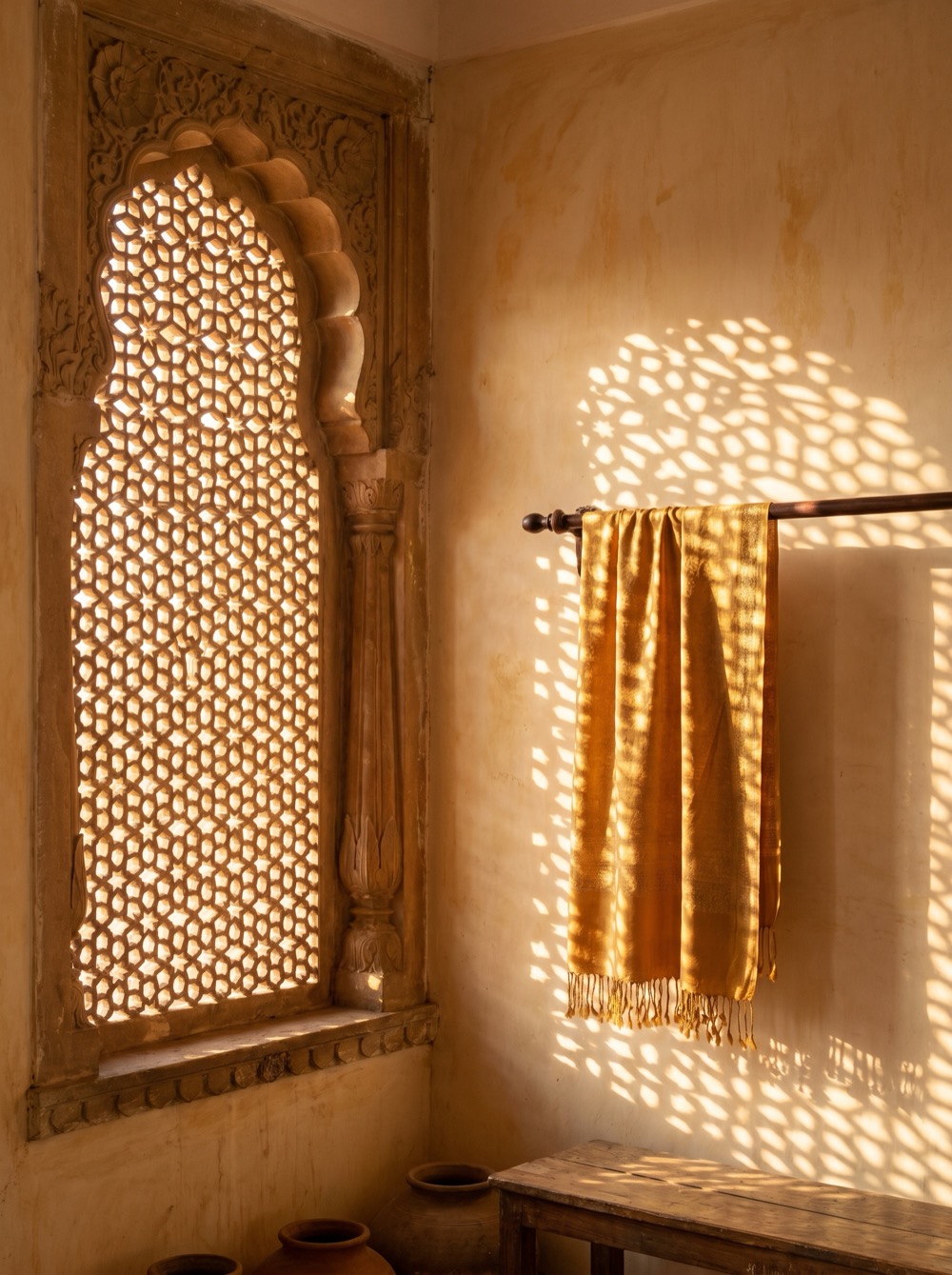 A saffron shawl hanging in the light of a carved Mughal lattice window